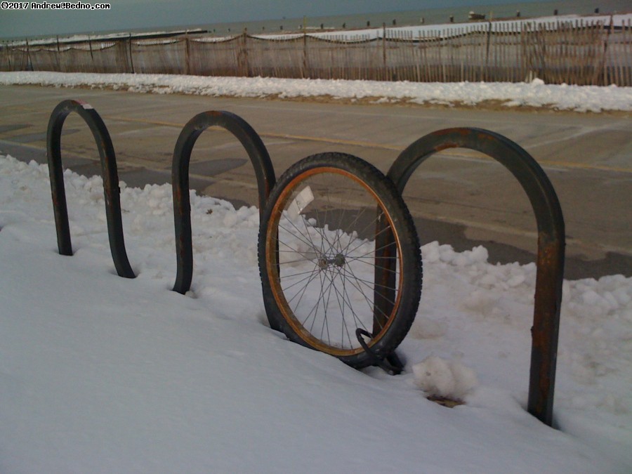 Lonely locked bike wheel in snow.